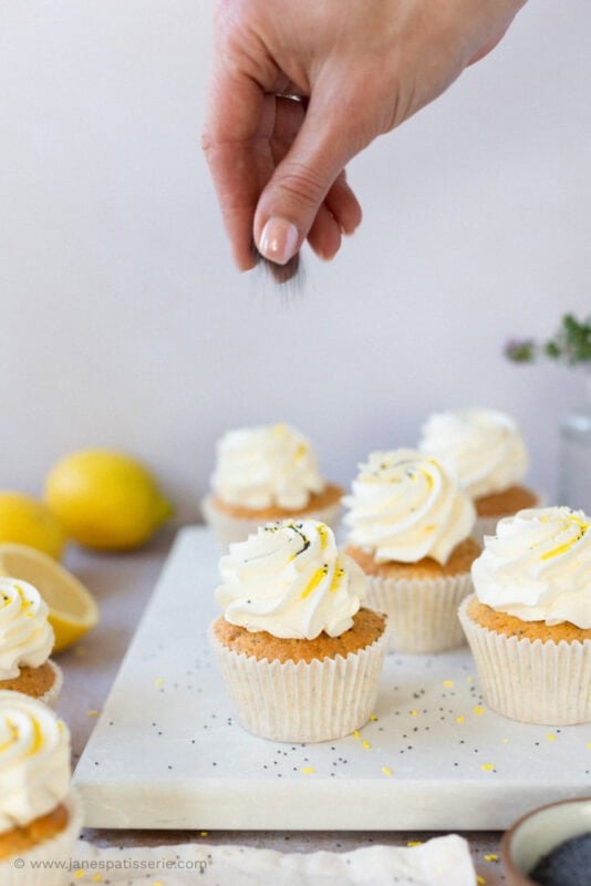 A hand sprinkling poppyseeds on lemon and poppyseed cupcakes