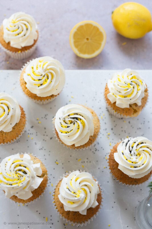 Multiple Lemon and Poppyseed cupcakes surrounded by Lemons and poppyseeds