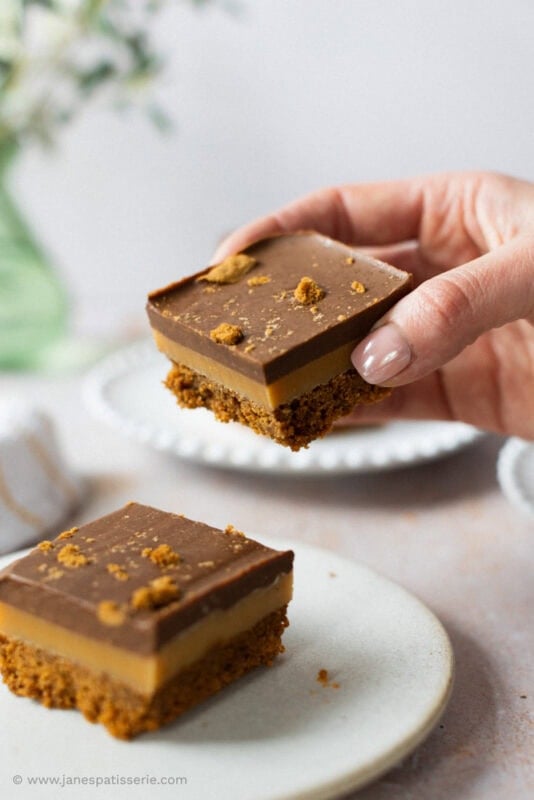 A hand taking a Biscoff Millionaires and one on a plate