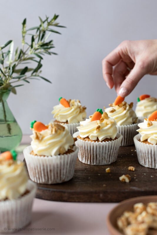 A hand placing a decoration on a Carrot cake cupcake