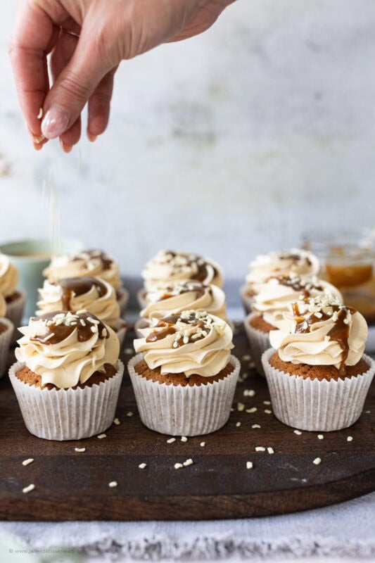 A hand sprinkling decoration onto a butterscotch cupcake