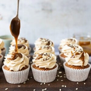 A spoon drizzling butterscotch sauce onto cupcakes