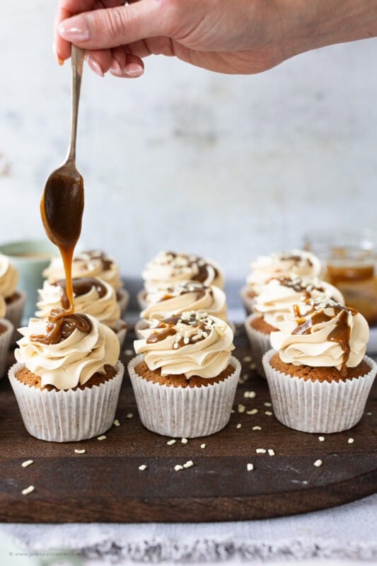 A spoon drizzling butterscotch sauce onto cupcakes