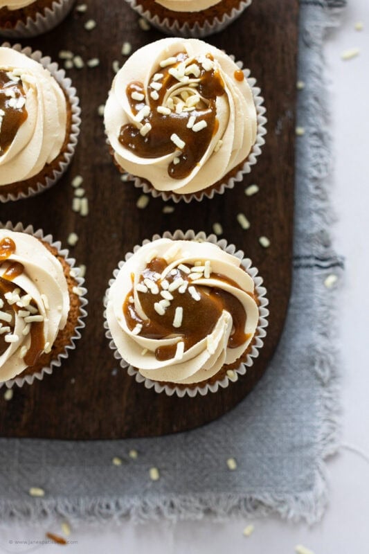 Decorated butterscotch cupcakes on a wooden chopping board