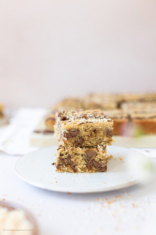 Two Coconut Chocolate Blondies stacked on a white plate