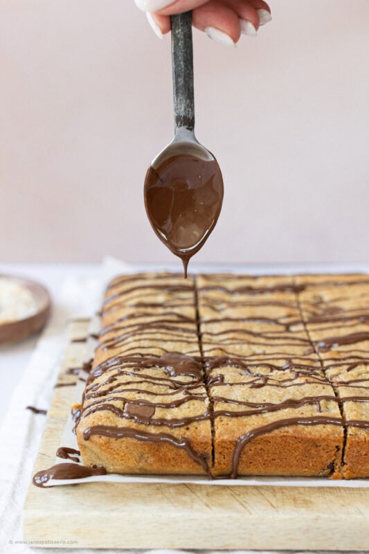 A spoon drizzling chocolate on Coconut Chocolate Blondies