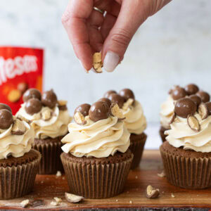 A hand crumbling Maltesers onto cupcakes