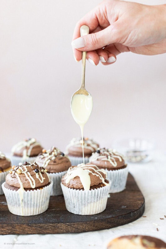 Drizzling white chocolate onto a marble cupcake
