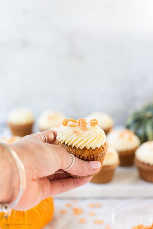 A hand holding a single Pumpkin Cupcake
