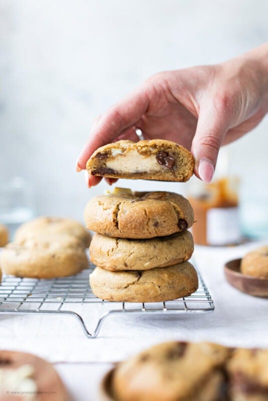A hand holding a Salted Caramel Cheesecake Cookie over a stack