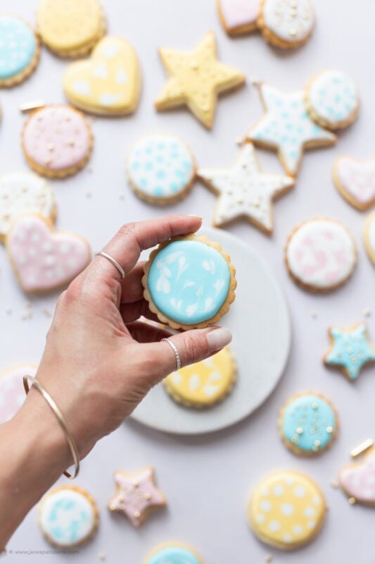 A hand holding a circle Sugar Cookie above a plate