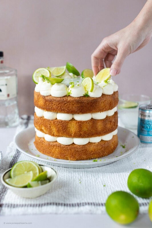 A hand placing limes on the top of Gin and Tonic Cake