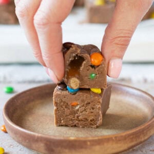 A hand taking a slice of microwave fudge from a plate