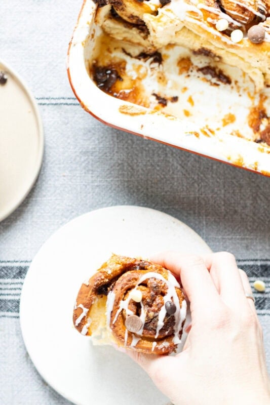 a hand holding a Sticky chocolate Sweet Roll on a plate