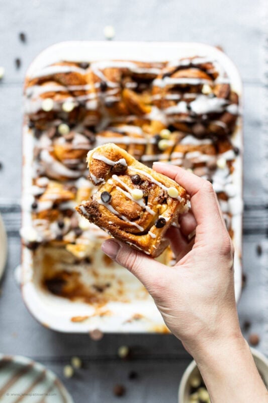 A hand holding a Sticky Chocolate Sweet Roll above the tray
