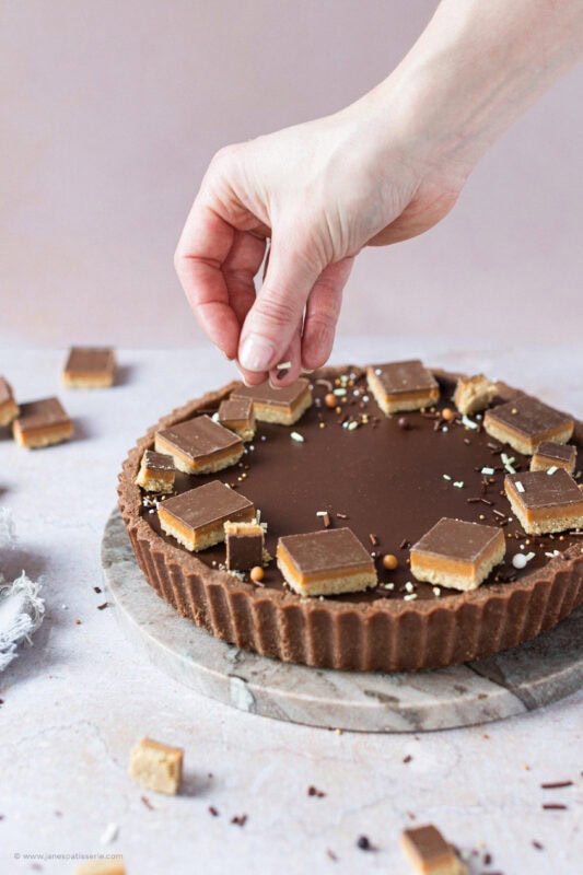 A hand placing the decoration on top of a Billionaires Tart