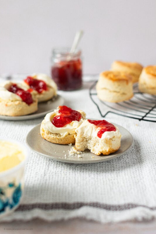Two classic buttery scones on a plate with a bite taken from one