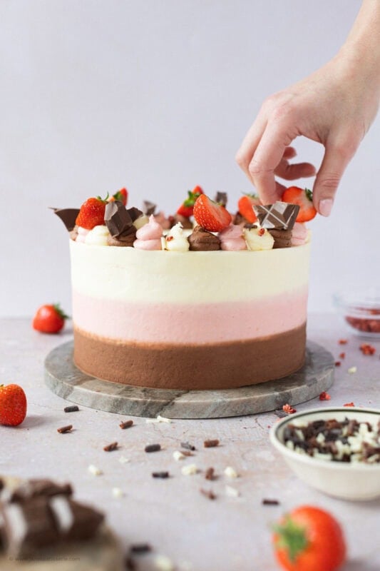 A hand placing the final touches of decoration to a Neapolitan Cake
