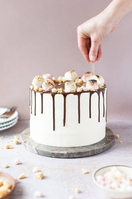 A hand decorating the S'mores Drip Cake