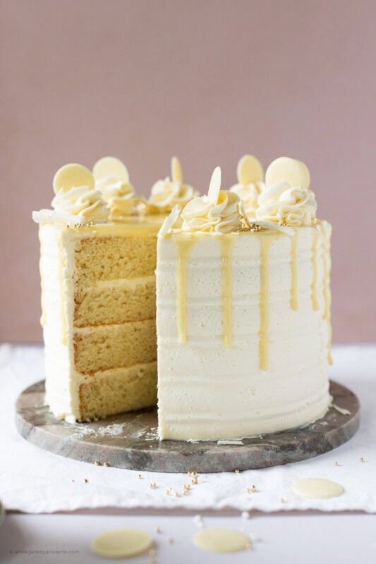 A slice missing from a White chocolate drip cake exposing the beautiful layers