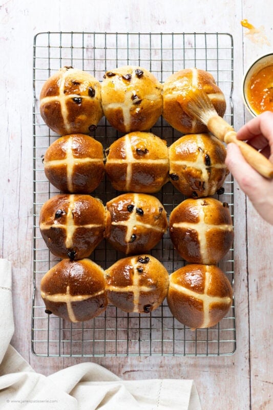 Glazing a cooling rack of freshly baked hot cross buns