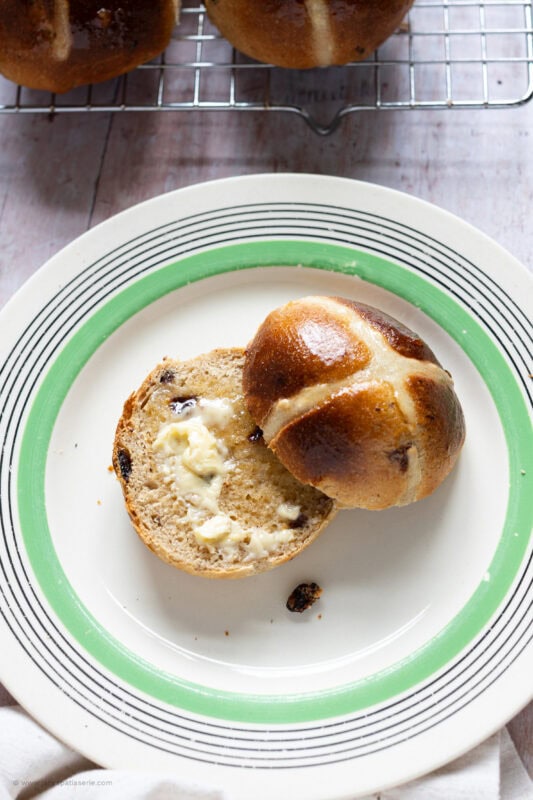 A single buttered hot cross bun on a plate