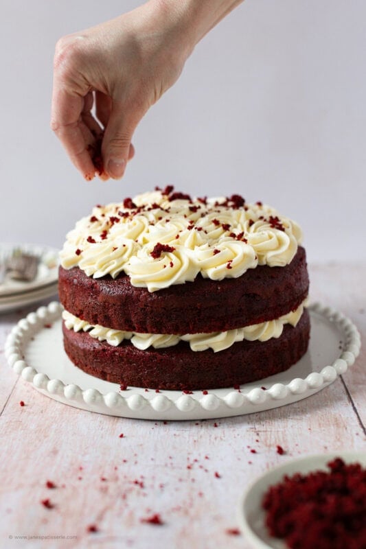 A hand decorating the finishing touches to the Red velvet cake